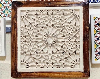 Könnte beinhalten: Ein quadratisches Wandkunstobjekt mit einem cremefarbenen, mehrschichtigen geometrischen Gittermuster aus komplexen Stern- und Polygonformen. Das zentrale Design ist von einem dunklen, polierten Holzrahmen mit sichtbarer Maserung umgeben.