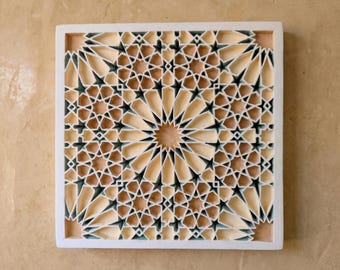 May include: A square wall art piece featuring a complex, multi-layered geometric pattern with star and polygon shapes. The design uses a palette of cream, beige, and dark blue-grey tones, framed by a solid white border with depth and shadows.