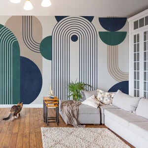Könnte beinhalten: Ein Wohnzimmer-Interieur mit einer modernen geometrischen Tapete mit Formen in Teal, Marineblau und Beige. Die Tapete hat ein gestreiftes Muster. Ein blauer Sessel, ein graues Ecksofa, eine Topfpflanze und eine Katze befinden sich im Raum.