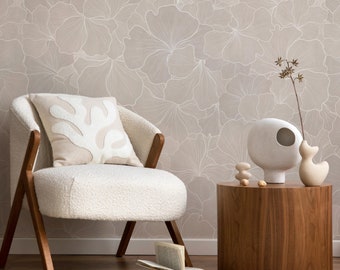 Op de afbeelding: Een witte fauteuil met een pluche textuur en een beige kussen met een wit bloemenpatroon staat voor een muur met een beige bloemenbehang. Een houten bijzettafel met een witte keramische vaas en een klein wit keramisch vogeltje staat naast de fauteuil.