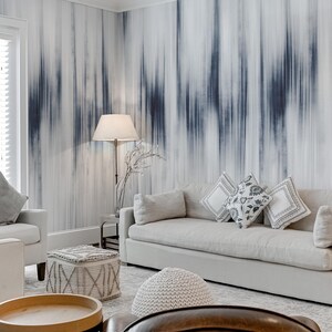 K&ouml;nnte beinhalten: Ein Wohnzimmer mit neutraler Farbpalette. Ein wei&szlig;es Sofa mit dekorativen Kissen steht vor einer Wand mit einem blau-wei&szlig;en abstrakten Design. Eine Stehlampe und ein wei&szlig;er Sessel sind ebenfalls zu sehen.
