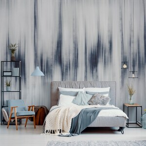 K&ouml;nnte beinhalten: Ein modernes Schlafzimmer mit einem grau gepolsterten Bett, einem hellblauen Stuhl und schwarzen Metallregalen. Die Wand zeigt ein gro&szlig;es abstraktes Wandbild in Grau- und Blaut&ouml;nen. Eine cremefarbene Decke und eine blaue Glasvase erg&auml;nzen die Einrichtung.