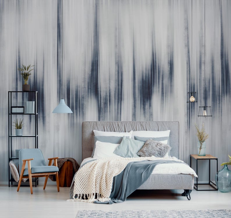 K&ouml;nnte beinhalten: Ein modernes Schlafzimmer mit einem grau gepolsterten Bett, einem hellblauen Stuhl und schwarzen Metallregalen. Die Wand zeigt ein gro&szlig;es abstraktes Wandbild in Grau- und Blaut&ouml;nen. Eine cremefarbene Decke und eine blaue Glasvase erg&auml;nzen die Einrichtung.