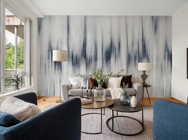 K&ouml;nnte beinhalten: Ein modernes Wohnzimmer mit einem grauen Sofa, zwei blauen Sesseln und zwei runden Couchtischen. Die Wand zeigt ein gro&szlig;es abstraktes Wandbild in Blau- und Wei&szlig;t&ouml;nen. Dekorative Kissen und Lampen vervollst&auml;ndigen den gem&uuml;tlichen Raum.