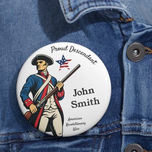 Op de afbeelding: Een witte button met een afbeelding van een soldaat uit de Amerikaanse Onafhankelijkheidsoorlog met een geweer. De button is voorzien van de tekst "Proud Descendant" en "John Smith" met een rood-wit-blauwe ster. De tekst "American Revolutionary War" staat er ook op.
