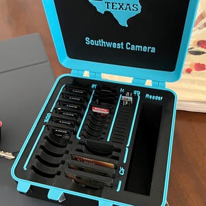 May include: A blue and black memory card case with the words "Texas Southwest Camera" on the lid. The case has slots for various memory cards, including SD, CF, and Sony Memory Stick.