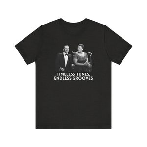Puede incluir: Camiseta negra con una foto de un hombre y una mujer cantando en micrófonos. El texto "TIMELESS TUNES, ENDLESS GROOVES" está impreso debajo de la foto.