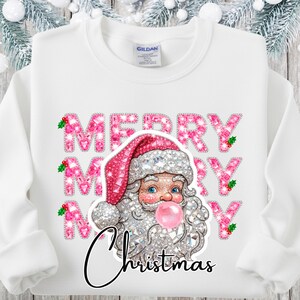 May include: White sweatshirt with a graphic of Santa Claus blowing a bubblegum bubble. The words "MERRY CHRISTMAS" are in pink, glittery letters. Santa wears a pink hat and has a silver beard.
