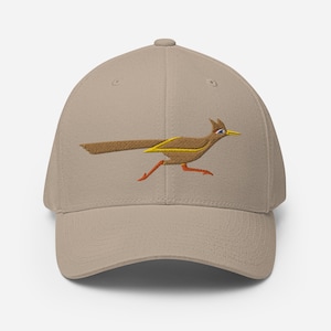 Può includere: Cappellino da baseball beige con ricamo di roadrunner. Il roadrunner è marrone con dettagli gialli e arancioni, raffigurato in piena corsa. Il cappellino ha una visiera curva e una forma strutturata. Un classico design dei cartoni animati.