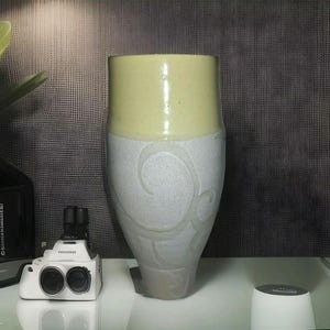 May include: A large, ceramic vase with a light yellow top and a white bottom. The vase has a swirling, embossed design on the white portion.
