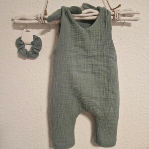 Könnte beinhalten: Ein grüner Baby-Strampler mit einem Schleifendesign am Oberteil. Der Strampler ist aus einem weichen, strukturierten Stoff gefertigt.