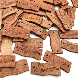 May include: A pile of brown wooden tags with the word "Handmade" and a heart design engraved on them. The tags have two holes for string or ribbon.