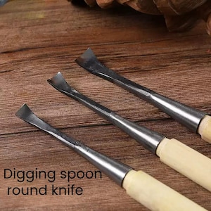 Puede incluir: Tres herramientas de talla con mango de madera y cuchillas de metal. Las cuchillas son curvas y puntiagudas, y los mangos son de madera clara. Las herramientas están dispuestas en fila sobre una superficie de madera. Digging spoon round knife