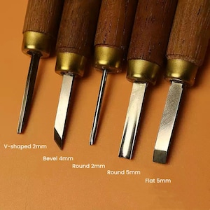 Może przedstawiać: Pięć narzędzi do rzeźbienia w drewnie z drewnianymi uchwytami i metalowymi ostrzami. Ostrza są oznaczone jako "V-shaped 2mm", "Bevel 4mm", "Round 2mm", "Round 5mm" i "Flat 5mm".