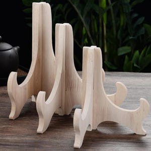 May include: Three wooden plate stands of varying sizes. The stands are made of natural wood and have a simple, elegant design. They are perfect for displaying plates, platters, or other decorative items.