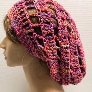 May include: A crocheted beanie hat in a multi-colored pattern of pink, orange, and purple.