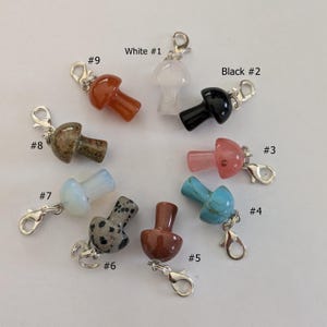 May include: Ten different colored stone mushroom charms with silver clasps. The charms are numbered 1 through 9. The colors include white, black, red, pink, turquoise, brown, gray, and green.