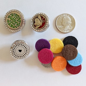 May include: Three silver car air freshener diffusers with different designs, including a butterfly, a heart, and a floral pattern. The diffusers are surrounded by ten colorful felt pads.
