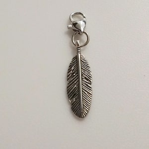 May include: A silver feather charm with a silver lobster clasp. The feather charm is detailed with lines and a central line running down the length of the feather.