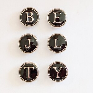 May include: Six black and silver round buttons with white letters spelling out the word "BELTY".