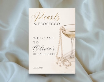 May include: A rectangular sign with a cream background featuring the text Pearls & PROSECCO WELCOME TO Olivia's BRIDAL SHOWER 22.03.2025. The design includes a graphic of a string of white pearls draped over a gold-rimmed champagne coupe glass.