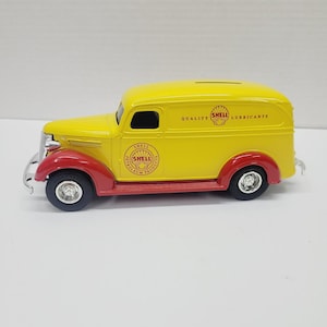 May include: A yellow and red vintage Shell Oil delivery truck toy. The truck features the Shell logo and the words "Quality Lubricants." The toy has black tires and chrome accents. A slot is visible on the roof.