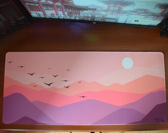 Puede incluir: Una cordillera de montañas rosa y púrpura con un sol blanco y pájaros negros volando sobre ella. El fondo es de color rosa claro. La alfombrilla de ratón es rectangular y tiene una superficie lisa.