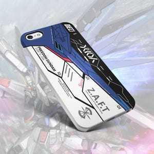 Può includere: Custodia per telefono bianca e blu con le scritte "FREEDOM GUNDAM" e "Z.A.F.T". La custodia presenta un design geometrico con dettagli rossi e neri. La custodia è progettata per uno smartphone.