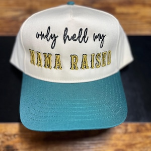 Könnte beinhalten: Weiß-tealfarbene Baseballkappe mit dem Text "only hell my mama raised" in Schwarz und Gold gestickt. Die Kappe hat einen tealfarbenen Schirm und einen tealfarbenen Knopf oben. Ein lässiges Accessoire.