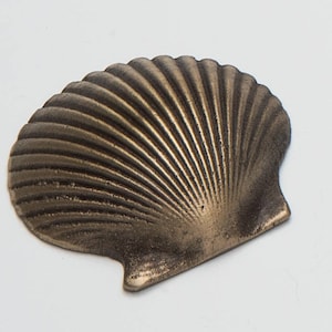 May include: A gold-colored metal seashell ornament with a detailed, ribbed texture.
