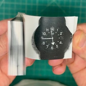 May include: A black and white image of a watch face with the text "SWISS ARMY" printed on it. The watch face has black hands and white numbers.