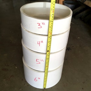 May include: A stack of four white plastic rings with measurements marked in inches. The rings are 3 inches, 4 inches, 5 inches, and 6 inches in diameter.