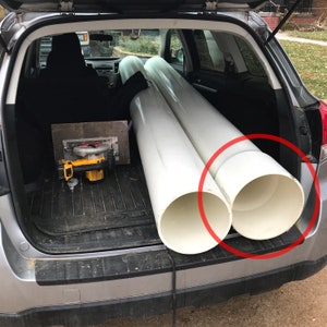 May include: The back of a silver car with the trunk open. Two large white PVC pipes are in the trunk. The pipes are about 10 inches in diameter.