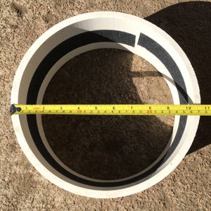 May include: A white circular drum with a black foam ring around the inside edge. A yellow measuring tape is wrapped around the outside of the drum, showing a measurement of 10 inches.