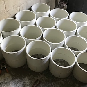 May include: A collection of white plastic cylinders of varying sizes, stacked and arranged in a semi-circular pattern on a concrete floor.