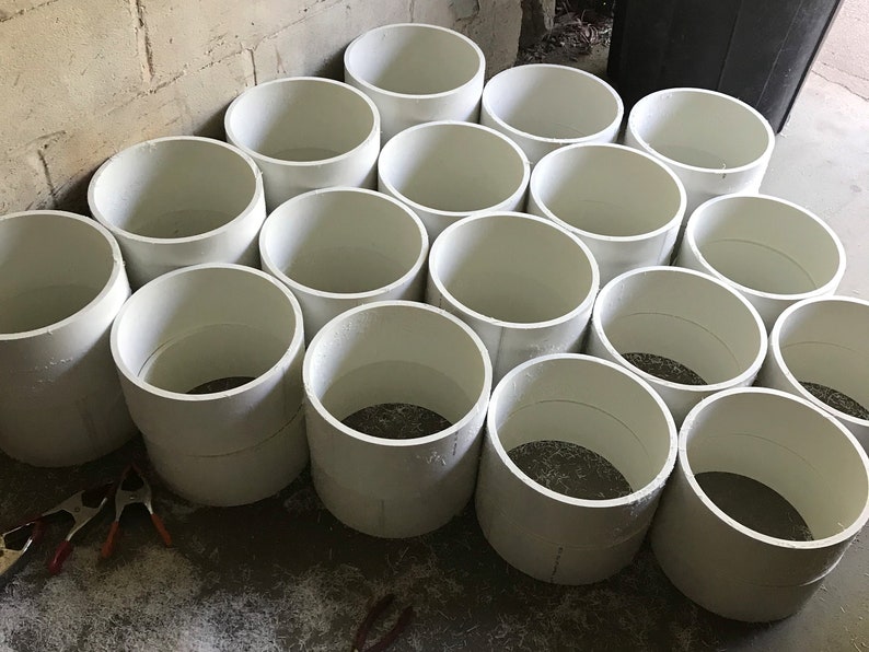 May include: A collection of white plastic cylinders of varying sizes, stacked and arranged in a semi-circular pattern on a concrete floor.