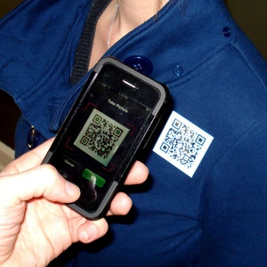 Könnte beinhalten: Ein schwarzes Smartphone mit einer blauen Hülle und einem QR-Code auf dem Bildschirm. Der Text "Take Picture" ist auf dem Bildschirm sichtbar. Das Telefon wird von einer Person gehalten, die eine blaue Jacke trägt.