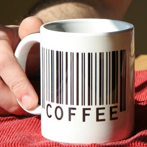 May include: White ceramic coffee mug with a black barcode and the word "COFFEE" printed on the front.