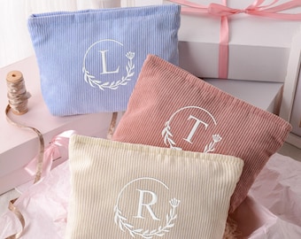May include: Three rectangular corduroy pouches in light blue, dusty rose, and cream. Each pouch features a white embroidered circular wreath design with a centered letter: L on the blue, T on the rose, and R on the cream pouch. The pouches are arranged together.