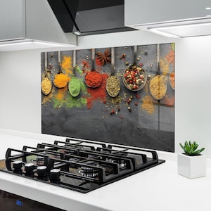Puede incluir: Un protector contra salpicaduras de cocina con una variedad de especias en cucharas de plata. Las especias son en tonos de amarillo, naranja, verde y rojo, con un fondo gris oscuro. Las cucharas están suspendidas, creando una disposición visualmente atractiva.