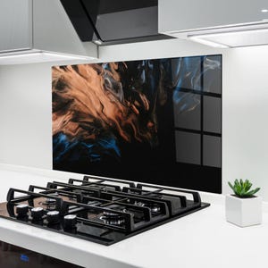 May include: A black glass kitchen backsplash with an abstract design in shades of brown, blue, and black. The backsplash is installed behind a black gas stovetop.
