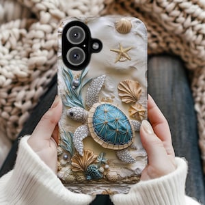 May include: A phone case featuring a 3D design of a sea turtle with a blue shell, surrounded by seashells, a starfish, and aquatic plants. The case has a textured, sandy background with a neutral color palette.