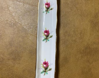 May include: A white rectangular dish with a gold rim and three pink roses with green leaves and stems.