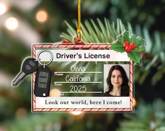 May include: A clear plastic Christmas ornament shaped like a driver's license. The ornament features a photo, the name "Olivia", and the state "California" with the year "2025". The text "Look out world, here I come!" is also included.