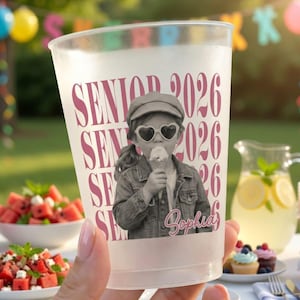 May include: A clear plastic cup with the words "SENIOR 2026" in pink. The cup features a black and white photo of a girl wearing heart-shaped sunglasses and eating ice cream. The name "Sophia" is written below the photo.