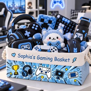 May include: A rectangular fabric storage basket with rope handles, labeled Sophia's Gaming Basket, featuring blue comic-style graphics of a trophy, headphones, controller, monitor, and handheld console, filled with gaming accessories and plush toys.