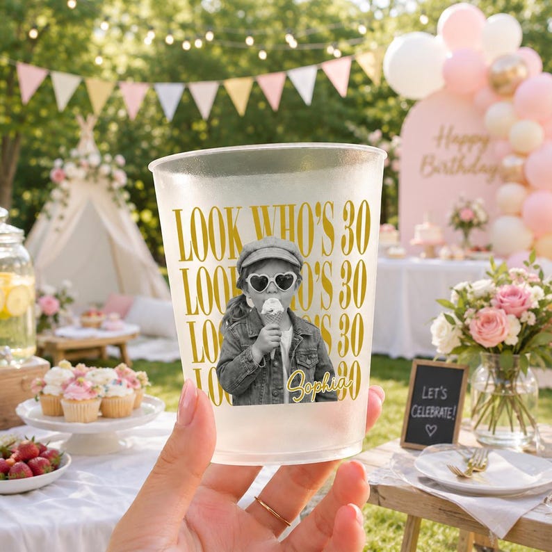 May include: A frosted plastic party cup featuring a black and white photograph of a child eating ice cream, wearing heart-shaped sunglasses and a denim jacket. The text "LOOK WHO'S 30" is printed in gold, with the name "Sophia" in gold script.