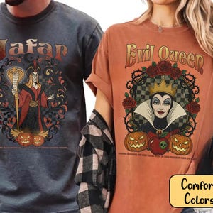 May include: Two t-shirts with graphic designs. One is a dark grey shirt with the word "Jafar" and a cartoon image of Jafar. The other is an orange shirt with the words "Evil Queen" and a cartoon image of the Evil Queen. Both shirts have pumpkins.