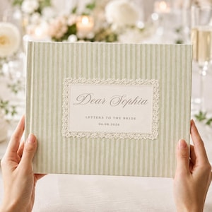 Peut inclure: Un livre rectangulaire avec une couverture à rayures verticales vert sauge clair et blanc. Une étiquette rectangulaire blanche centrale présente une bordure en dentelle décorative et le texte Dear Sophia, LETTERS TO THE BRIDE, 06.08.2026.