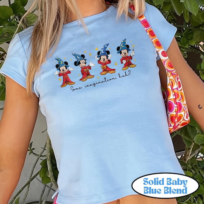 May include: Light blue t-shirt featuring a graphic of Mickey Mouse dressed as a wizard, with the text "Some imagination, huh?" The shirt is labeled "Solid Baby Blue Blend".